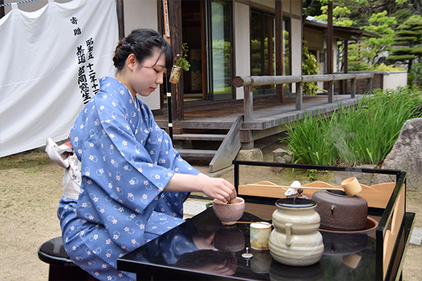 あでやかな着物姿でお点前を披露する女子学生。日本庭園を眺めながらの茶会は、ふれあいフェスタならでは。