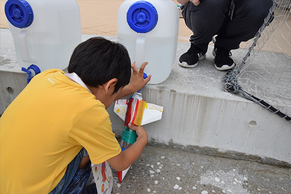 水の量を自分で調整する子どもたち。「水を入れ過ぎると上手く飛ばないかもしれないよ」と女子学生がアドバイス。