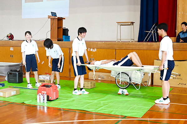 避難所に常備された担架や発電機などの資機材を紹介する五日市高等学校の生徒