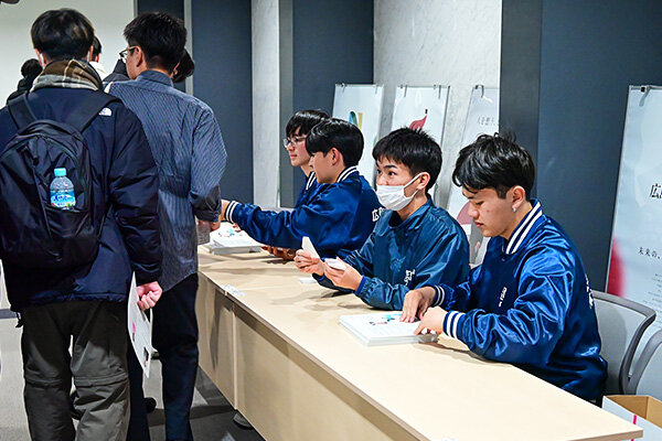 受付で来場者にレジュメと抽選番号を手渡す様子