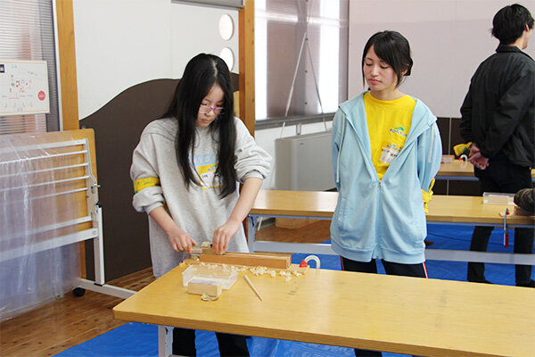 学生がサポートする中、木材をカンナで削り、箸の形に仕上げていく