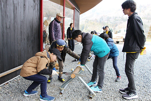 のこぎりを使って丸太を切り、木のメダルを作る
